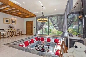 A spacious living area with a central seating arrangement, a dining table, and a large window with curtains. - Hi At Home Villa 4 (Pattaya)