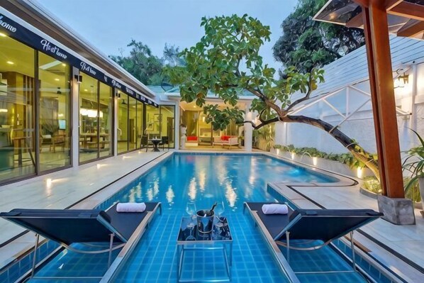 A swimming pool with lounge chairs, a covered seating area, and a glass-enclosed building. - Hi At Home Villa 4 (Pattaya)