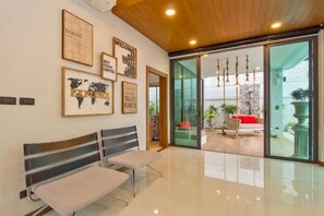 A hotel lobby with a reception desk, framed welcome signs, and a view of the outdoor seating area. - Hi At Home Villa 4 (Pattaya)