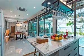 A modern kitchen with a marble countertop, a dining area with a table and chairs, and a large window overlooking a pool. - Hi At Home Villa 4 (Pattaya)