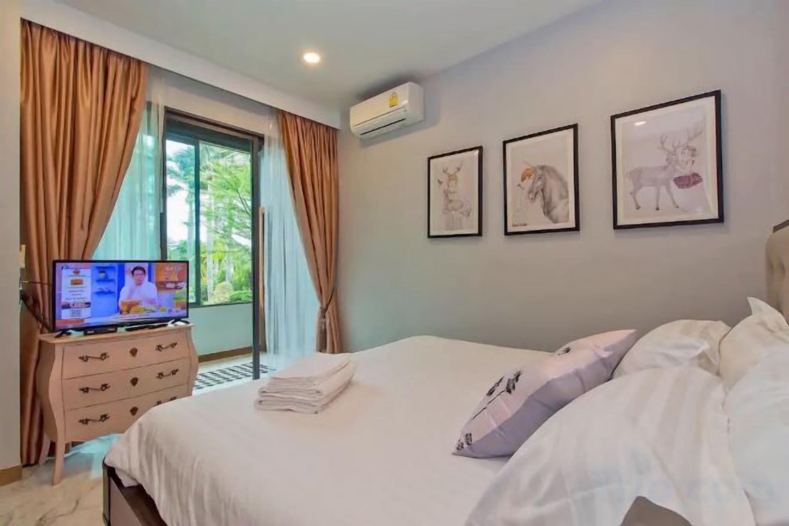 A hotel room with a bed, a television on a dresser, and a window with curtains.