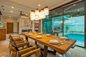 A dining area with a long wooden table set for six, surrounded by chairs. - Hi At Home Villa 4 (Pattaya)