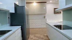 A modern kitchen with white cabinetry, a black refrigerator, and a built-in stove. - Warm 4-Bedroom Apartment At Vinhomes Skylake (Hanoi)