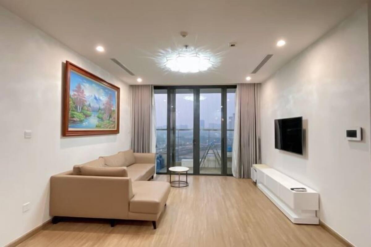 Sala de estar moderna com sofá, um quadro, televisão e vista através de grandes portas de vidro.