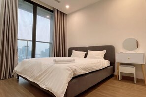 Une chambre d’hôtel moderne avec un grand lit, une table de chevet et une vue sur les gratte-ciel de la ville, grâce à de grandes fenêtres du sol au plafond.