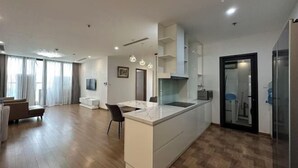 A modern apartment with a kitchen island, a dining area, and a living room with a sofa and a TV. - Warm 4-Bedroom Apartment At Vinhomes Skylake (Hanoi)