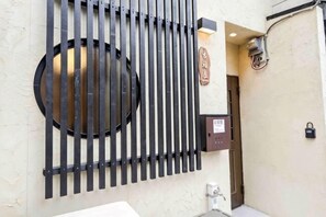 Un cancello metallico con barre verticali e un oblò circolare, un portaluce a parete e una porta con serratura.