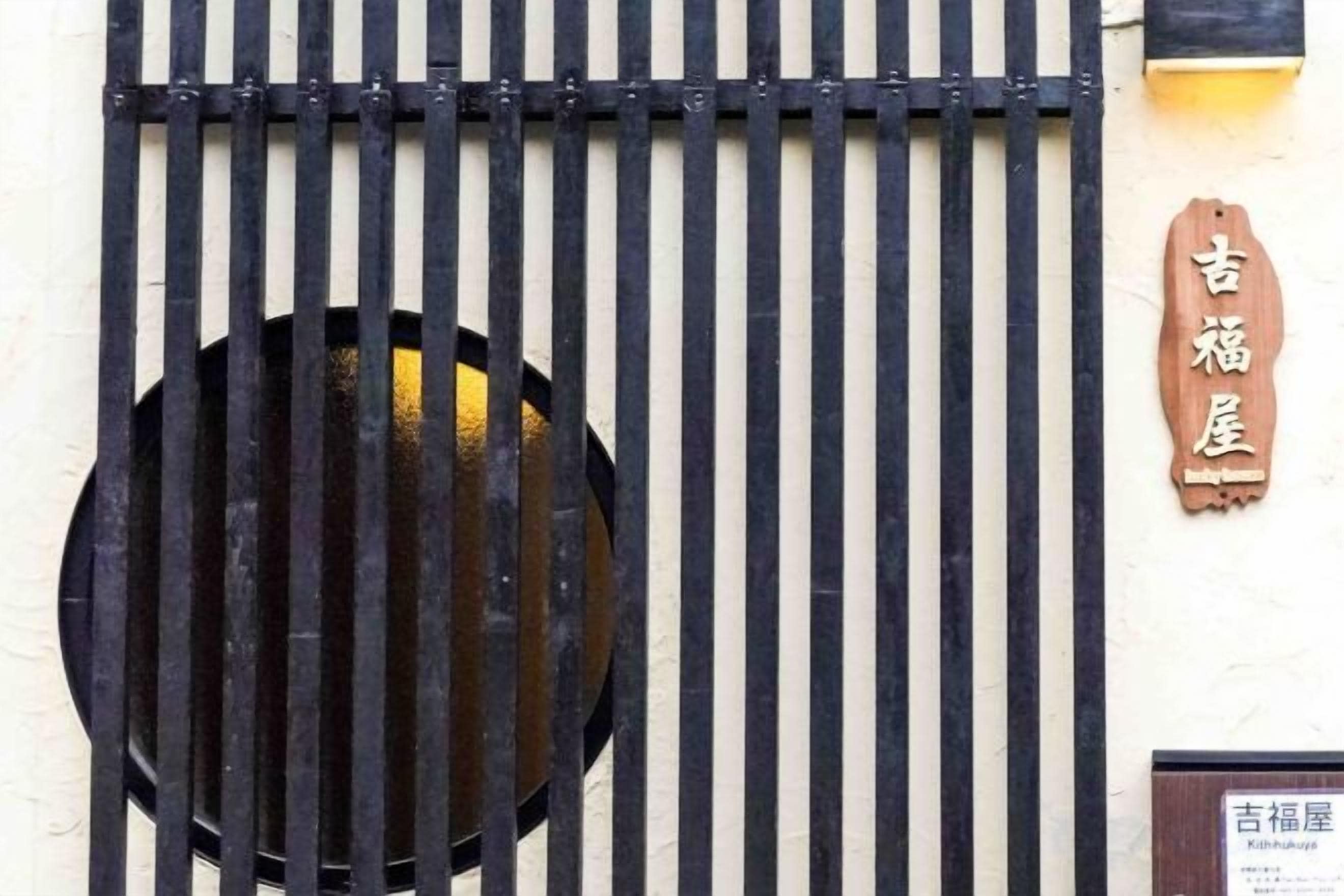 A traditional Japanese gate with vertical bars and a circular window.
