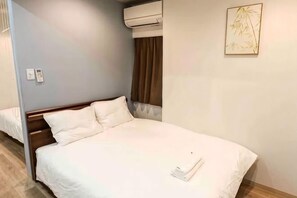 Hotellihuone, jossa on yksi sänky, yöpöytä, seinään asennettu ilmastointilaite ja seinällä oleva taulu.