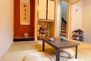Perinteinen japanilainen huone, jossa on tatamimatto, matala pöytä teekupit ja -astiastot valmiina, sekä liukuovi, joka johtaa toiseen huoneeseen.