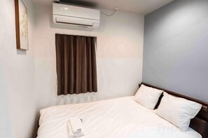 A hotel room with a bed, a window with curtains, an air conditioning unit, and a wall-mounted artwork. - Yoshifukuya (Osaka)