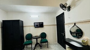 A small room with a black wardrobe, two green chairs around a small table, a black counter, a wall-mounted TV, and a mirror. - Phú Gia Hotel Phu My Quan 7 (Ho Chi Minh City)