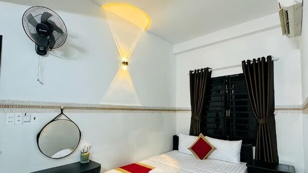 A hotel room with a bed, bedside table, mirror, wall-mounted fan, and curtains. - Phú Gia Hotel Phu My Quan 7 (Ho Chi Minh City)
