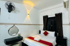 Una habitación de hotel con cama, mesita de noche, espejo, ventilador de pared y cortinas.