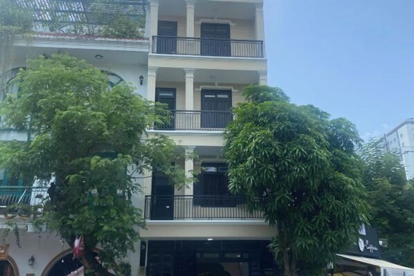 Un immeuble à plusieurs étages, doté de balcons, avec un arbre devant.