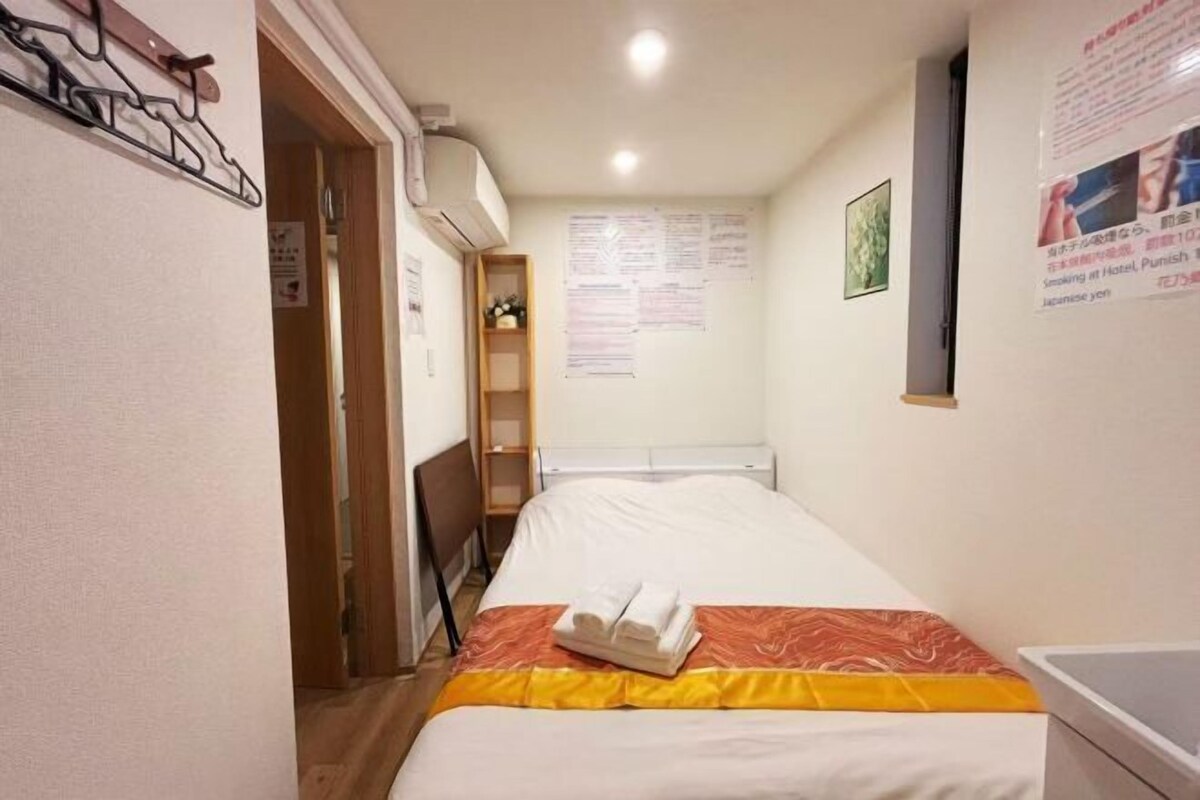 A hotel room with a bed, a small shelf, and a wall with informational posters.