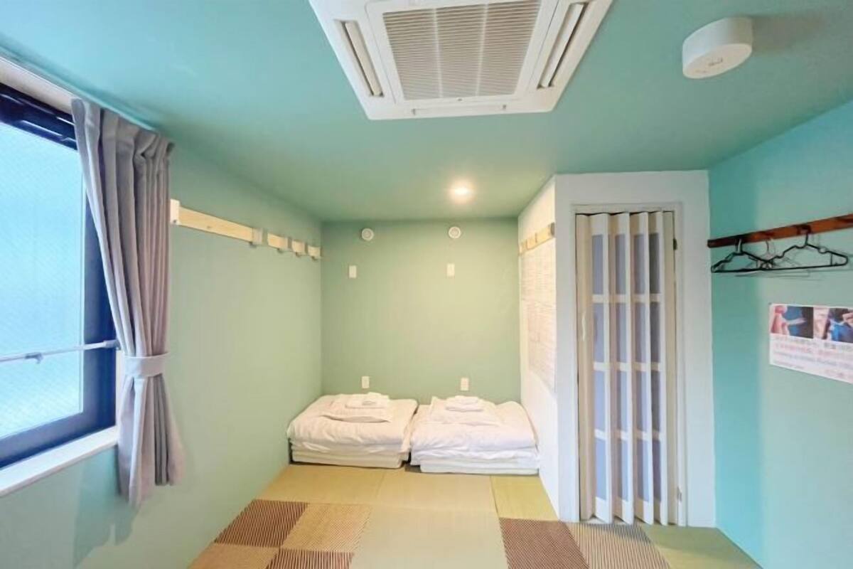 Una habitación de hotel pequeña y sencilla con cama, ventana con cortinas, aire acondicionado de pared y puerta con panel de vidrio corredera.