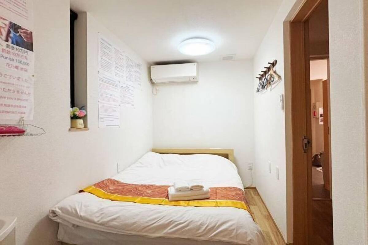 Una habitación de hotel pequeña y estrecha con una cama individual, un aire acondicionado de pared y una puerta de madera.