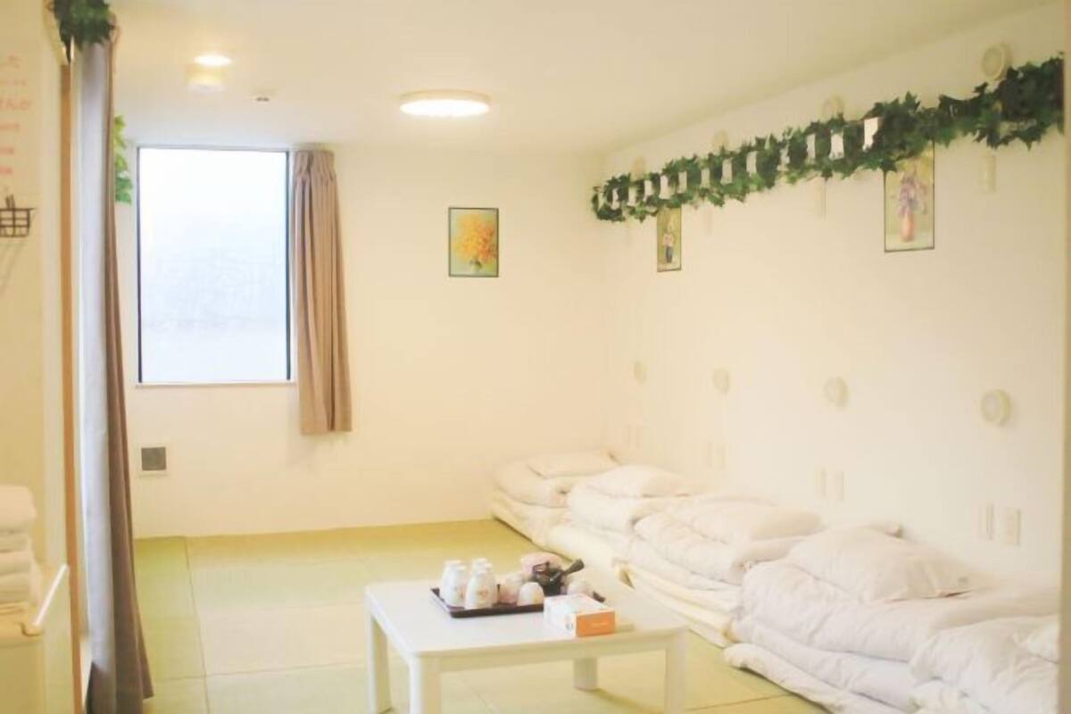 Una habitación con un ventanal grande, un sofá blanco, una mesita con artículos de aseo, y una pared decorada con cuadros y una guirnalda.