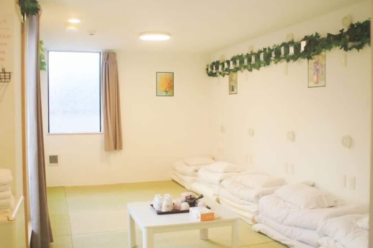 A room with a large window, a white sofa set, a small table with toiletries, and a wall with framed pictures and a garland.