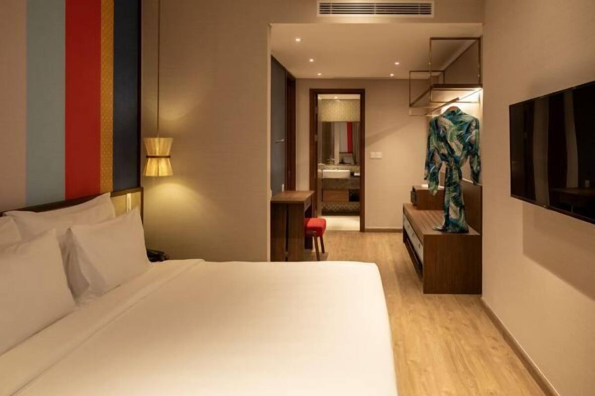 Habitación de hotel con una cama grande, un escritorio con silla, un televisor montado en la pared y un espejo sobre el escritorio.