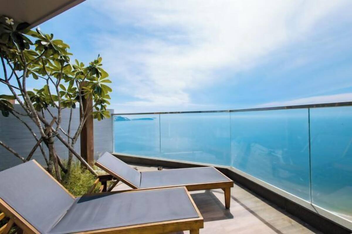 Un balcón con dos sillones de descanso y barandilla de cristal con vista al mar.