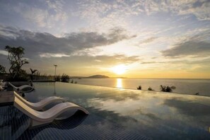 Une piscine à débordement offrant une vue imprenable sur le coucher de soleil sur l’eau.