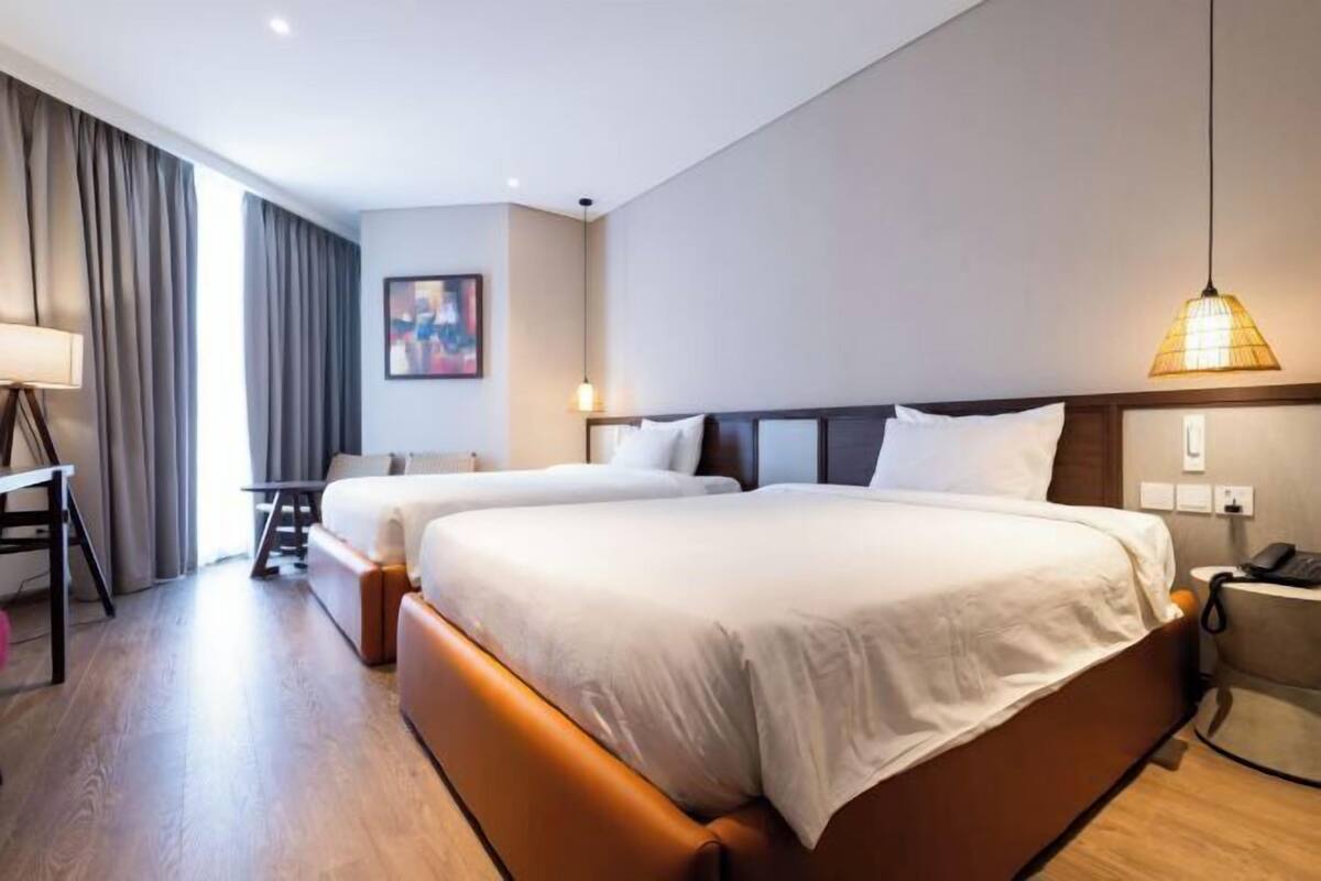 Habitación de hotel con dos camas, un escritorio, una silla y una lámpara.