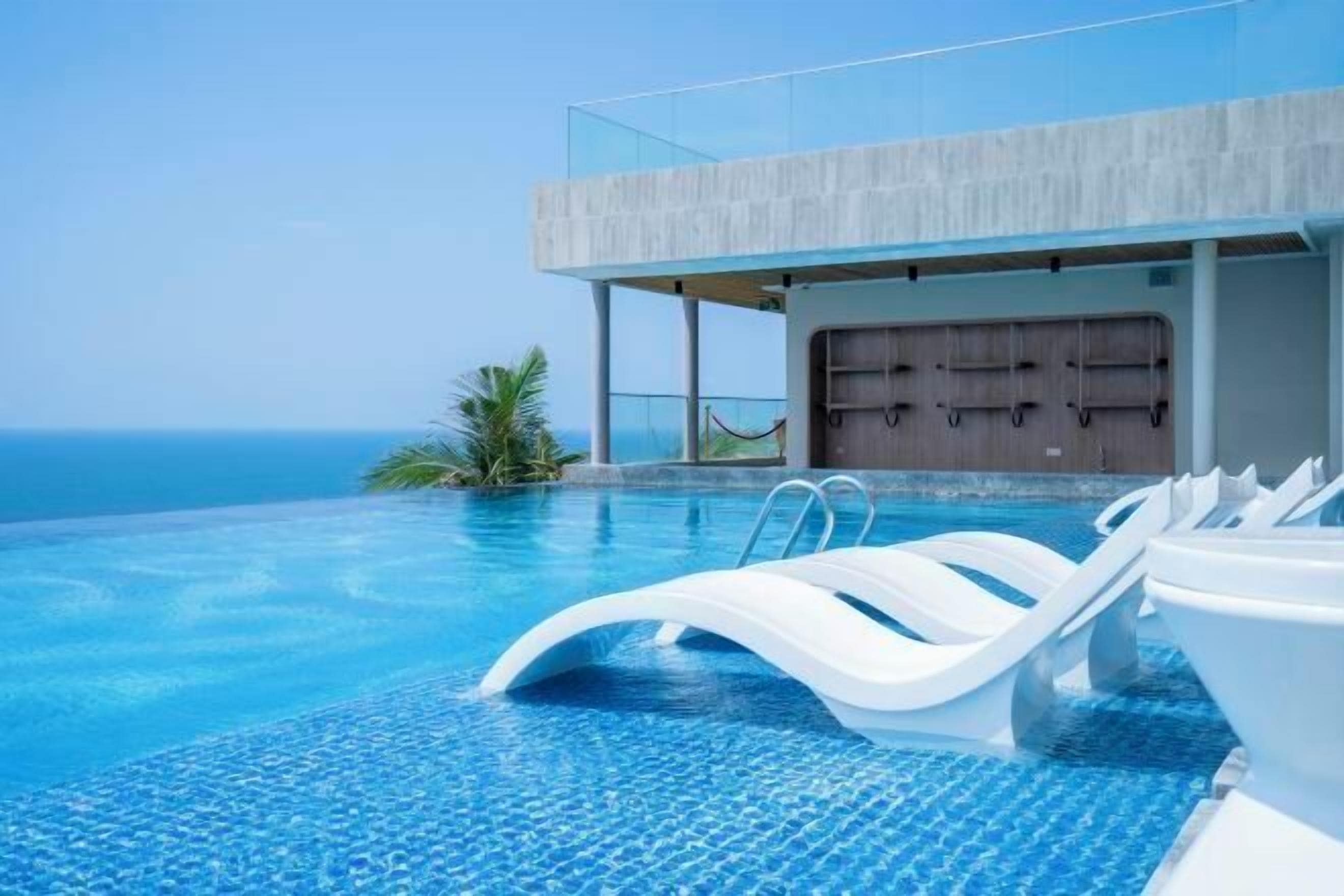 A modern infinity pool with clear blue water, white lounge chairs, and a view of the ocean.