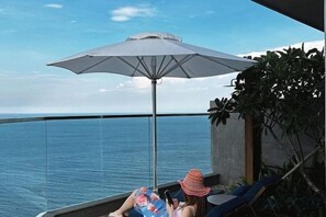 Un balcon avec vue sur la mer, un grand parasol et une personne se détendant.
