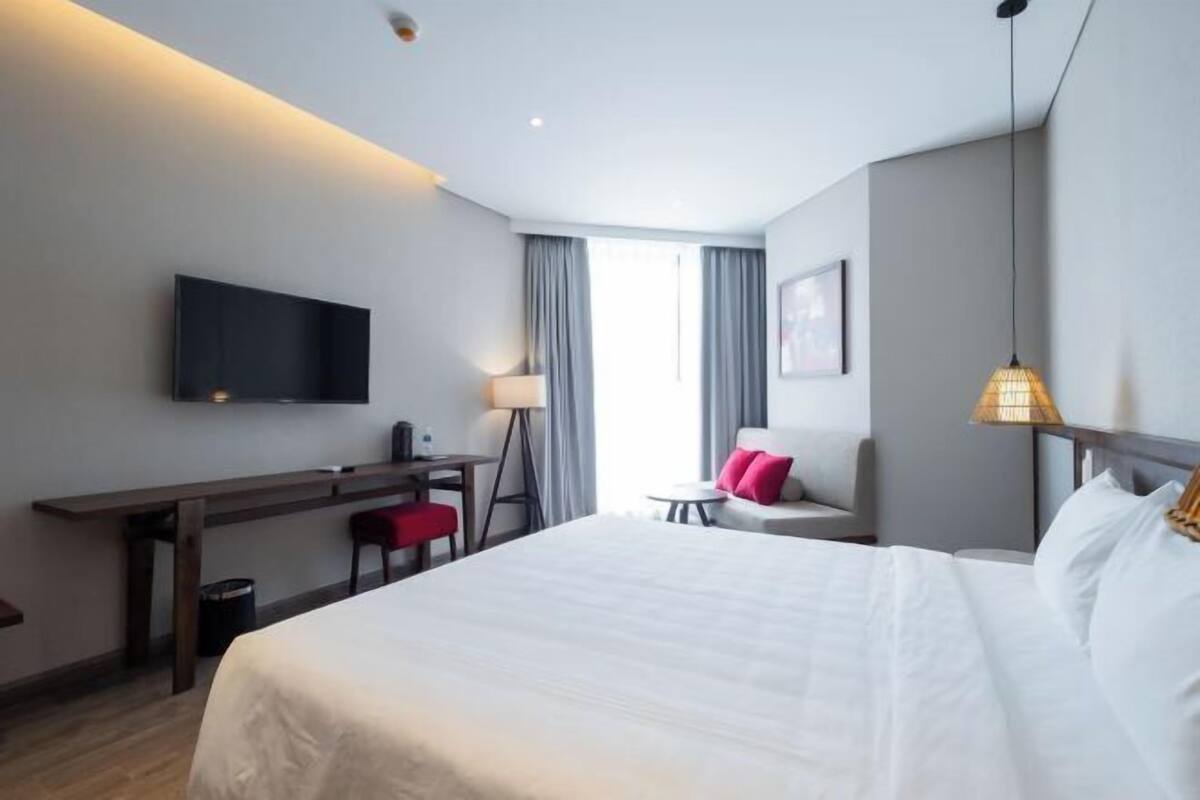 Habitación de hotel con una cama grande, un escritorio, una silla, un televisor montado en la pared y una lámpara.