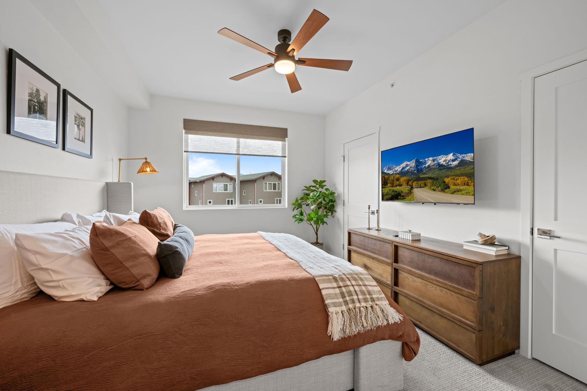 A bedroom with a bed, a ceiling fan, a window, a dresser, and a TV on the wall.
