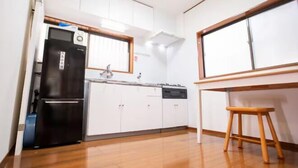 A compact kitchen with white cabinets, a black refrigerator, a dishwasher, and a wooden stool. - Shinjuku Everlasting Cabin (Tokyo)