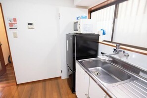 A compact kitchen with a refrigerator, microwave, sink, and wooden flooring. - Shinjuku Everlasting Cabin (Tokyo)