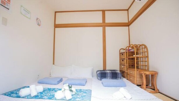 Een net opgemaakt bed met blauw-witte beddengoed, een houten hoofdbord en een rieten opbergmeubel.