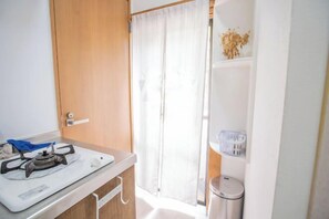 A compact kitchenette with a gas stove, a small sink, and a trash bin. - Shinjuku Everlasting Cabin (Tokyo)