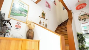 A reception area with a wooden desk, a framed landscape picture, a vase with dried flowers, and a staircase with wooden steps. - Shinjuku Everlasting Cabin (Tokyo)