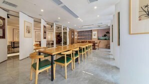 A spacious dining area with long wooden tables and green cushioned chairs, a kitchen in the background, and framed artwork on the walls. - Resort Hotel on the landscap (Xiamen)