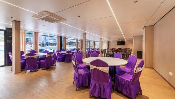 Ein Konferenzraum mit runden Tischen und violetten Stühlen, großen Fenstern und einem modernen Deckenstil.