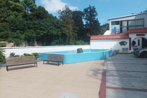 Ett utomhusområde med en pool, bänkar och en byggnad med ett rött tak.