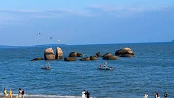 A beach with large rocks, boats, and people.