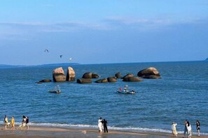 A beach with large rocks, boats, and people. - Resort Hotel on the landscap (Xiamen)