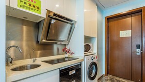 A compact kitchen with a stainless steel range hood, a built-in microwave, a washing machine, and a sink. - TUXI INTERNATIONAL APARTMENT (Guangzhou)