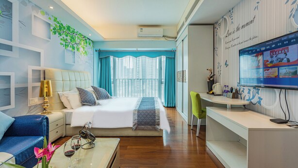 A modern hotel room with a large bed, a desk with a computer, a TV, and a view of the city through large windows. - TUXI INTERNATIONAL APARTMENT (Guangzhou)