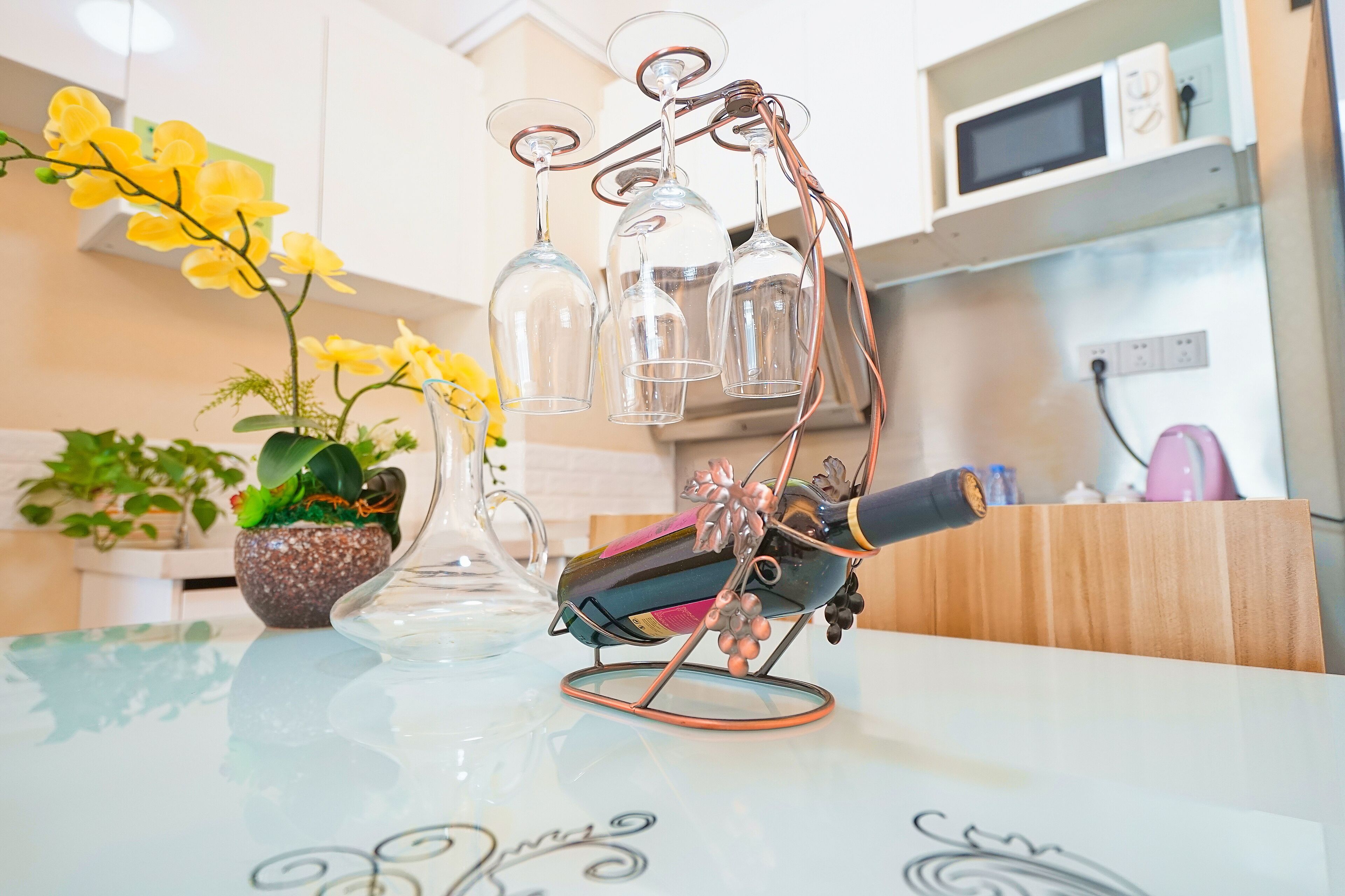 A kitchen with a glass table, a wine bottle, and a decorative metal stand holding wine glasses.
