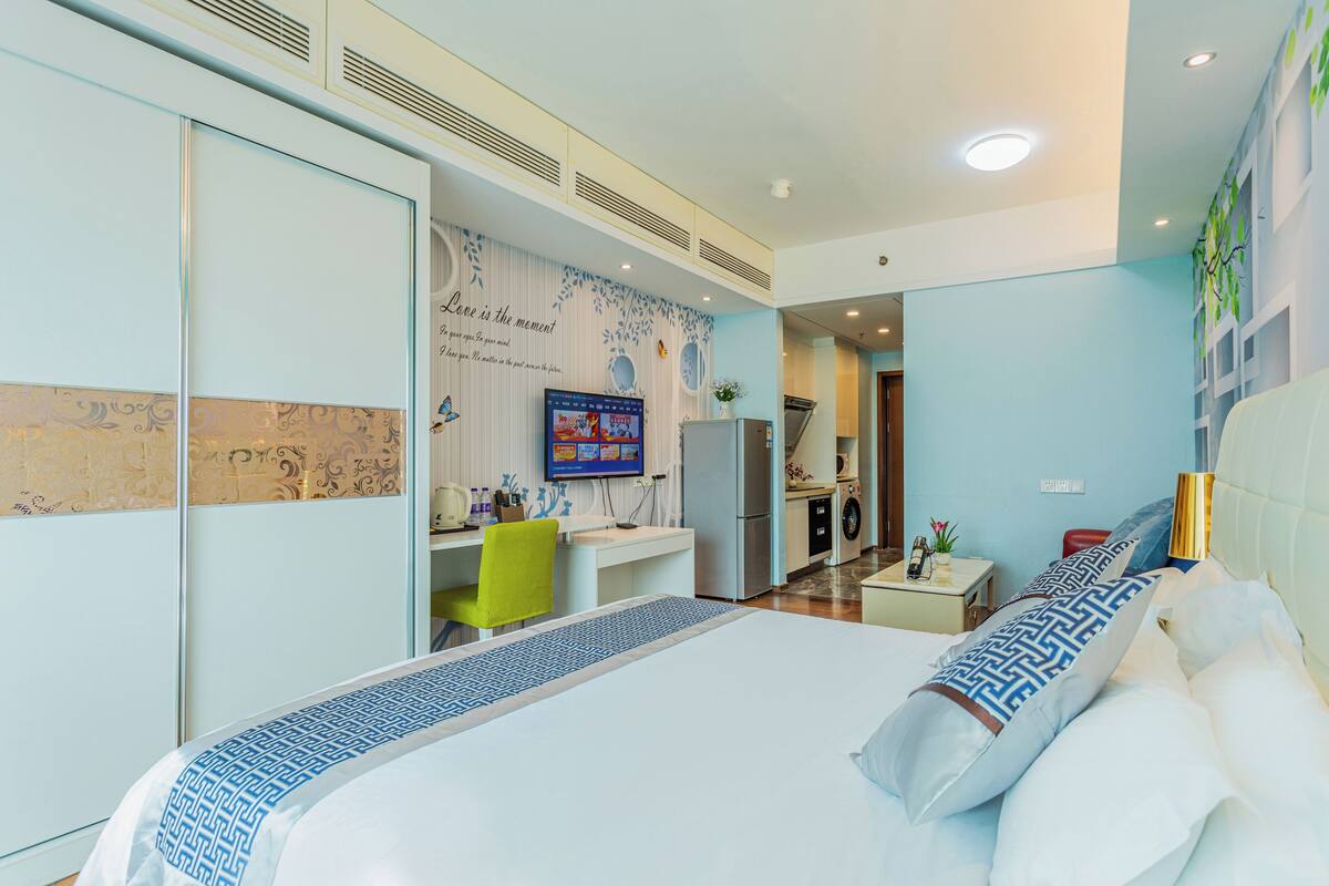 Ein Hotelzimmer mit Bett, Schreibtisch, Stuhl, Fernseher, Küchenzeile und Kleiderschrank.