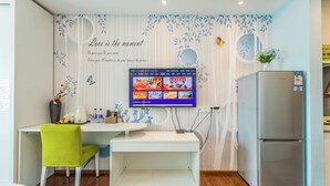 A modern kitchen with a flat-screen TV mounted on the wall, a refrigerator, a dining table with a green chair, and decorative wall art. - TUXI INTERNATIONAL APARTMENT (Guangzhou)