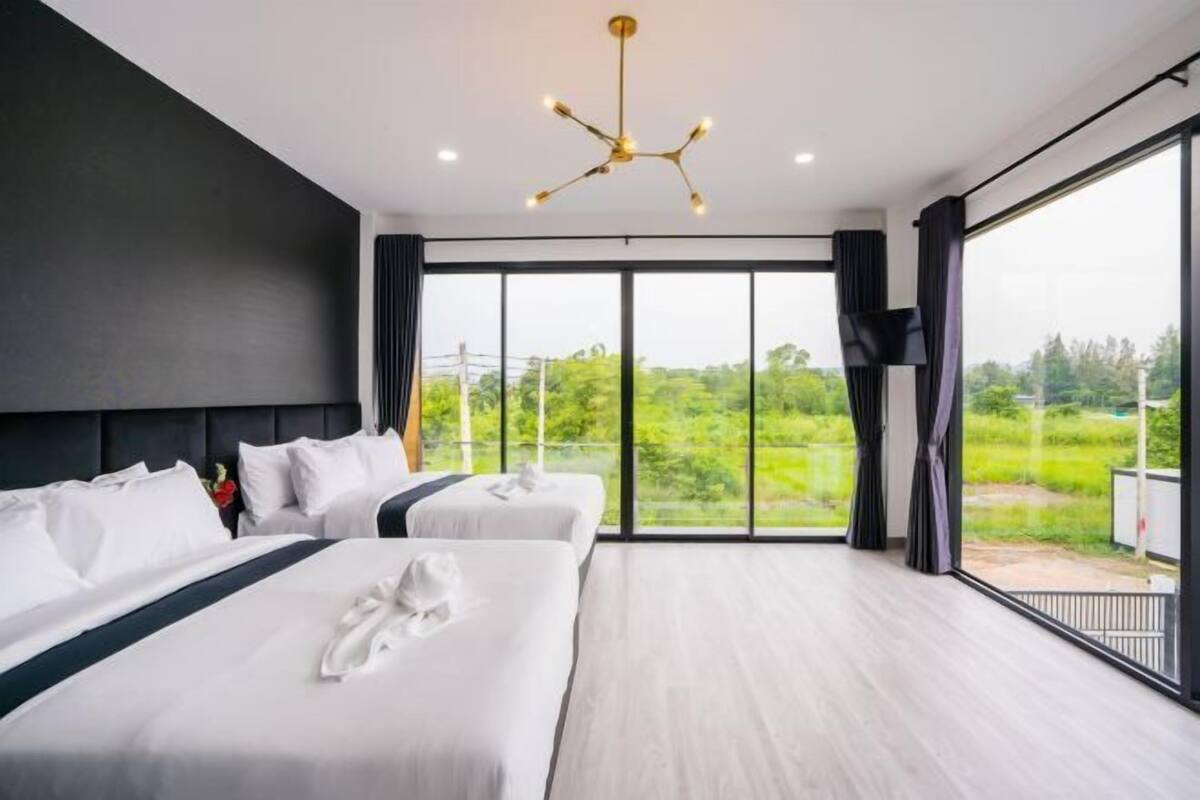 A modern hotel room with two beds, a large window, and a ceiling light fixture.