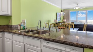 A kitchen with granite countertops, a dishwasher, and a window overlooking a balcony. - Relax in Rare Low-Density Luxury – Marisol 3BR Beachfront Condo (Panama City Beach)