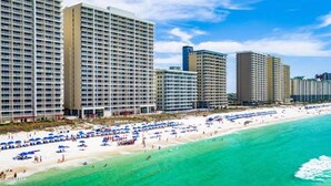 A beachfront hotel with multiple high-rise buildings, a sandy beach with umbrellas, and clear turquoise water. - Relax in Rare Low-Density Luxury – Marisol 3BR Beachfront Condo (Panama City Beach)